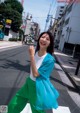 A woman in a blue jacket and green pants crossing the street.