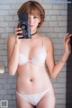 A woman in a white bra and panties holding a camera.