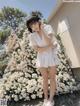 A woman standing in front of a wall of white flowers.