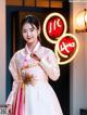 A woman in a pink and white hanbok standing in front of a neon sign.