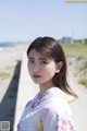 A woman in a white and pink kimono standing on a beach.